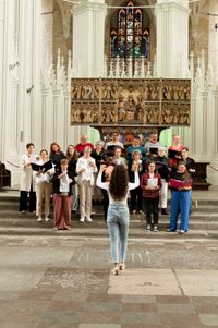 Foto des Chores in einer Kirche, die Chorleiterin dirigiert im Vordergrund